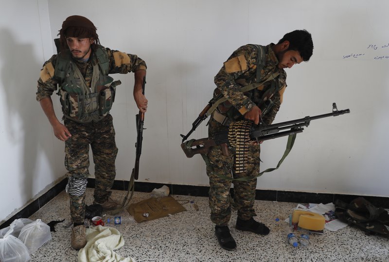 In this July 22, 2017 file photo, an Arab fighter, left, and Kurdish fighter, right, who fight together with the U.S.-backed Syrian Democratic Forces (SDF), hold their weapons as they prepare to move to the front line to battle against the Islamic State militants, in Raqqa, northeast Syria. 