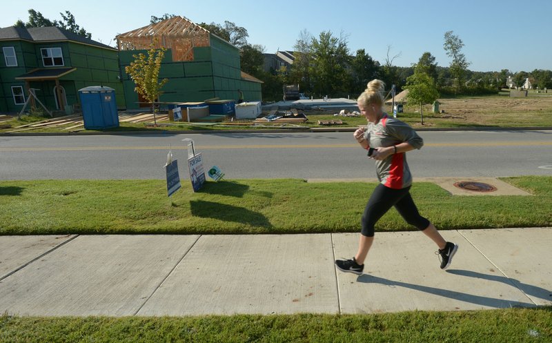 A runner makes her way along Salem Road on Saturday past houses being built south of Wedington Drive in Fayetteville. Northwest Arkansas builders are unable to keep pace with demand for houses in the area, and are branching out into smaller communities in the region.