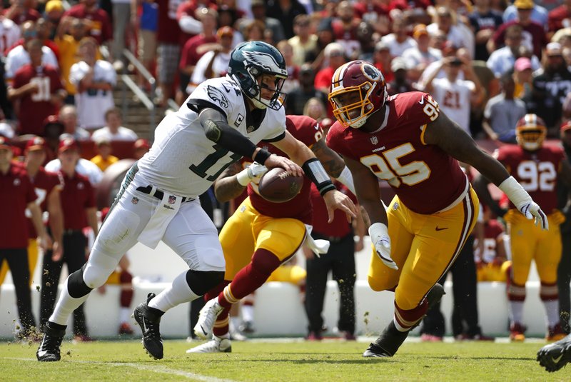 Philadelphia Eagles quarterback Carson Wentz, left, tries to outrun Washington Redskins defensive end Jonathan Allen (95) and outside linebacker Preston Smith as he looks for a receiver in the first half of an NFL football game, Sunday, Sept. 10, 2017, in Landover, Md. 