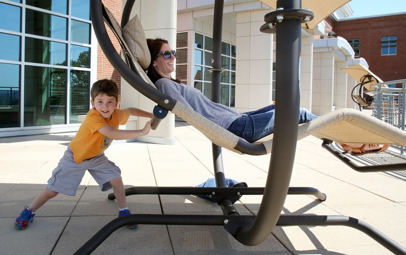 Cruze Kirk, 4, pushes his mother, Katie, in one of the swinging chairs Monday on the rooftop patio and garden area at Fayetteville Public Library. The library is currently in its preliminary design phase for expansion onto property next door.
