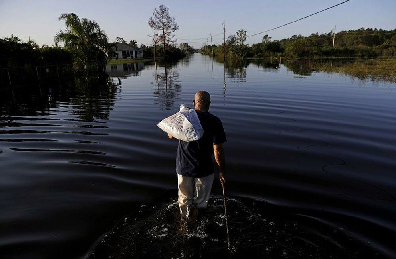 Jean Chatelier wades to work at a supermarket Tuesday in Fort Myers, Fla., after going home to get his uniform. The Publix store where he is employed will reopen today. “I want to go back to work,” said Chatelier, who walked about a mile each way through knee-high water. “I want to help.” 