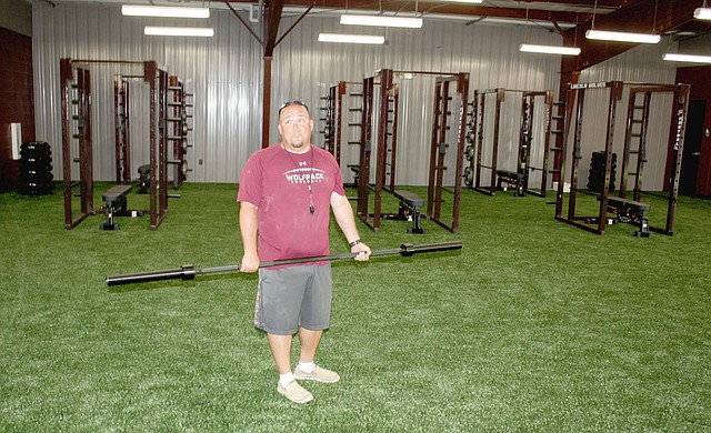 MARK HUMPHREY ENTERPRISE-LEADER Lincoln head football coach Don Harrison carries a barbell as the Wolves move weight lifting equipment into their new Football Fieldhouse on Tuesday, Sept. 5.