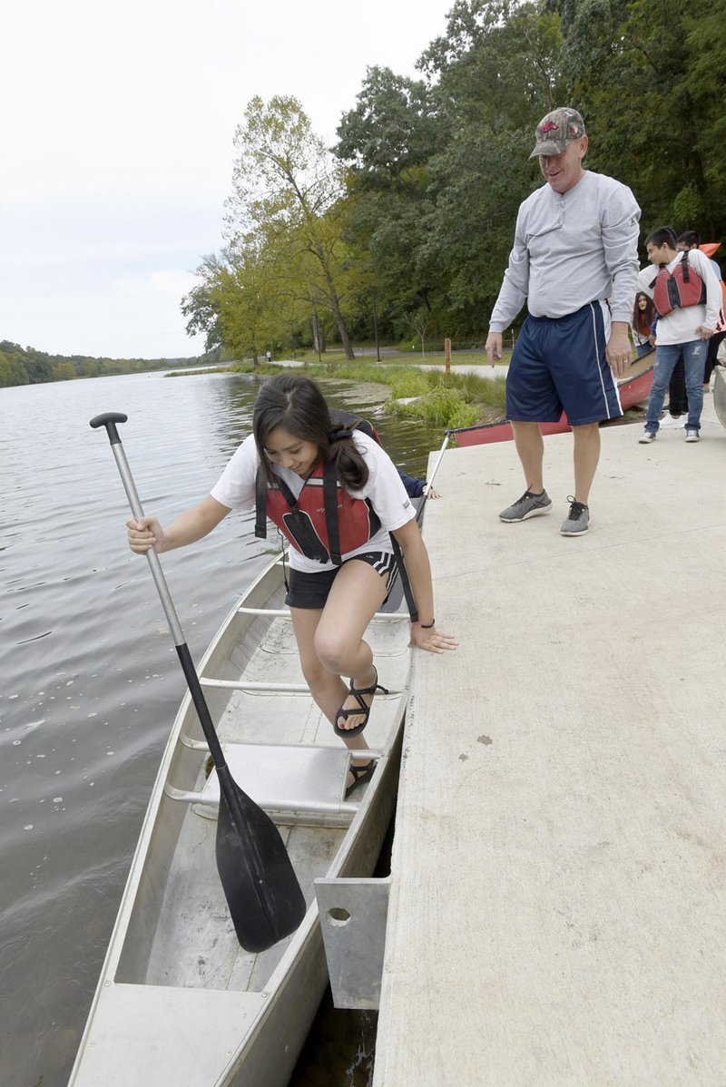 NWA Democrat-Gazette/FLIP PUTTHOFF Ahtziri Maldonado, a student at Heritage High School, boards a canoe Tuesday during an outdoor education class taught by Tom Olsen (right) at Lake Atalanta Park in Rogers. Parts of the park were damaged by flooding in April.