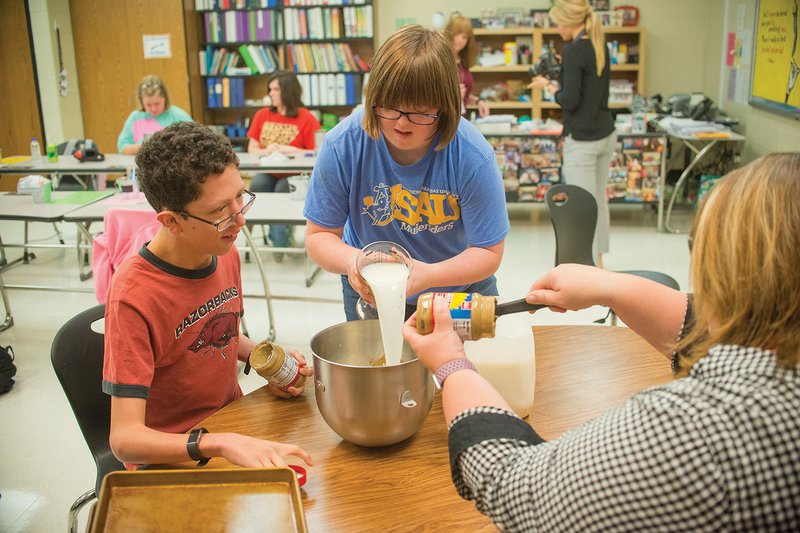Students Robert Lewis, from left, Olivia Dixon and Shelley Moore mix a batch of K9 Crackers in their community-based instruction class at Cabot High School. Dixon said her favorite part of making the dog treats is mixing the ingredients, while Lewis said he enjoys bagging the crackers and feeding them to his furry friends.