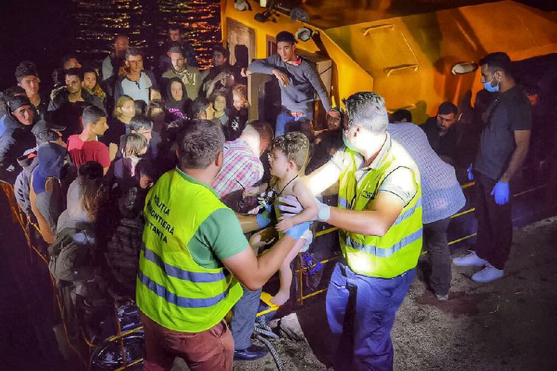 In a photo provided by the Romanian border police, officers carry a child early Wednesday as they help rescue migrants in the Black Sea port of Constanta, Romania. 