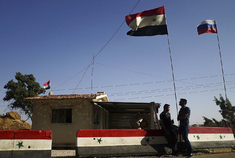 People wait under waving Syrian and Russian flags Wednesday at a de-escalation zone checkpoint to receive Russian food aid near Homs, Syria.