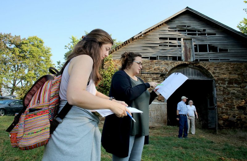 Lauren Lambert and Katie Murphy, graduate students at the University of Louisiana at Lafayette, review architectural documents Friday in front of the horse barn at Fitzgerald Station in Springdale. Students from the university will come up with plans for the site, which once was a stagecoach stop on the Butterfield Overland Express mail route.