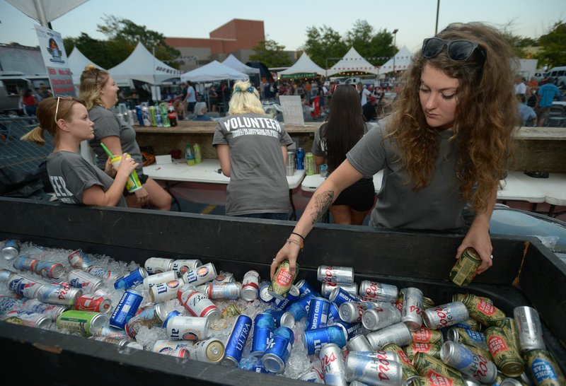 NWA Democrat-Gazette/ANDY SHUPE Chelsea Arenado of Bentonville reaches into an ice-filled container of drinks Wednesday while serving people in the main beer garden near the performance stage in the Walton Arts Center parking lot during the annual Bikes, Blues & BBQ motorcycle rally in Fayetteville. Arenado was volunteering to sell drinks to benefit Open Avenues in Rogers, a charitable organization helping adults with intellectual differences.