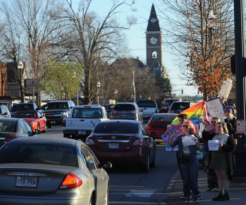 NWA Democrat-Gazette/ANDY SHUPE Participants hold signs and flags at College Avenue and Dickson Street on Feb. 24 during a rally in reaction to the state Supreme Court decision finding the city&#8217;s ordinance extending protections to lesbian, gay, bisexual and transgender residents violates state law.