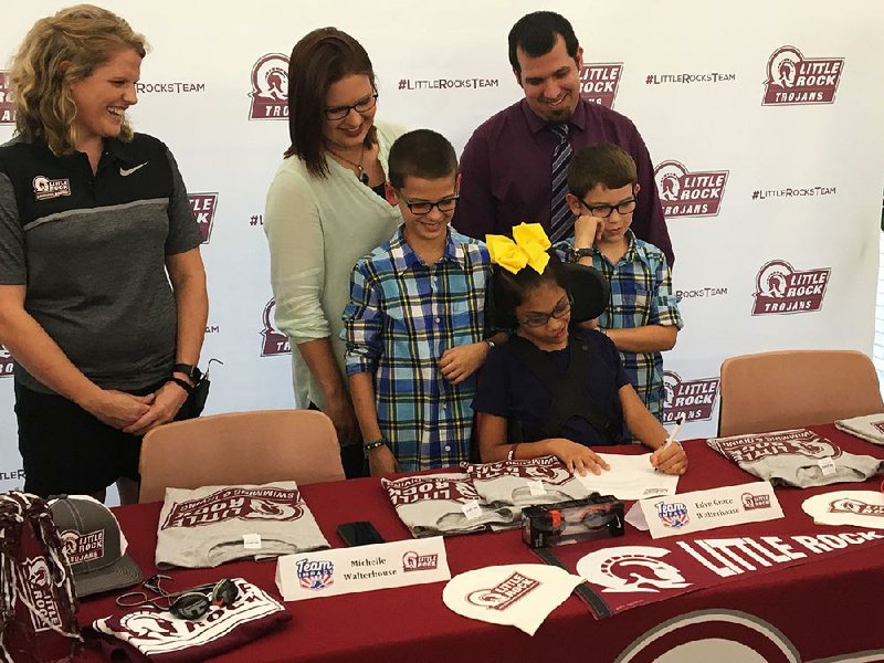Edyn Grace Walterhouse, 9, of Little Rock, is surrounded by her family and University of Arkansas at Little Rock swimming and diving Coach Amy Burgess as she signs a national letter of intent with the Trojans on Wednesday. Edyn is part of a program that pairs children facing life-threatening and chronic illnesses with collegiate athletic teams.