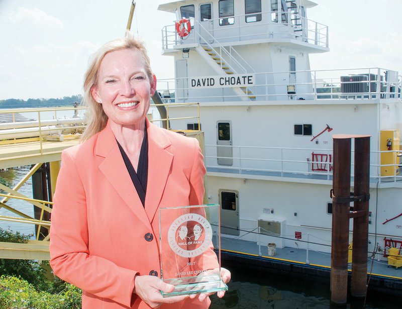 Penny Choate stands in front of the Arkansas River holding David Choate’s Arkansas River Hall of Fame award plaque. She described her husband, who died earlier this year after a long battle with brain cancer, as a caring person and a brilliant businessman.