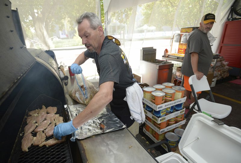 NWA Democrat-Gazette/ANDY SHUPE Randy Adams (left) places marinaded chicken breasts on the smoker Friday in the official barbecue tent during the annual Bikes, Blues & BBQ Motorcycle Rally in Fayetteville. Organizers put their interest in tailgating and making food for others to use in creating the first official event food option.