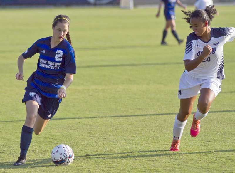 Photo courtesy of JBU Sports Information John Brown junior forward Jastin Redman, left, dribbles down the field as Oklahoma Wesleyan&#8217;s Kayla Beaver gives chase during Tuesday&#8217;s match in Bartlesville, Okla. OKWU defeated JBU 3-1.