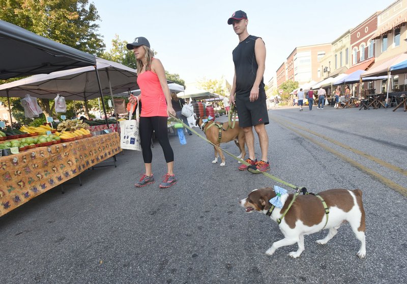 Tara and Mark Kinsley shop Sept. 16 with their dogs Buster (left) and Peter at the Bentonville Farmers Market. Northwest Arkansas businesses see steady traffic of customers with dogs on Saturday during farmers market hours