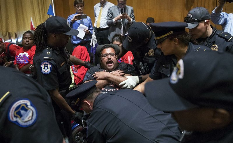 An activist opposed to the Republican health care bill is removed by U.S. Capitol Police on Monday after protesters disrupted a Senate Finance Committee hearing on Capitol Hill.