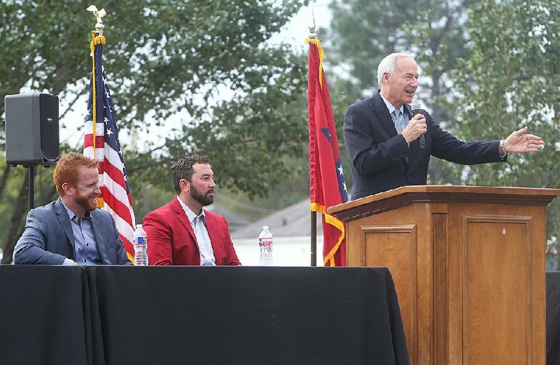 Shaun Keefe (from left) and Morgan Wiles listen Wednesday as Gov. Asa Hutchinson speaks in Mountain Pine about the partners’ plans for an industrial park in the Garland County town.  