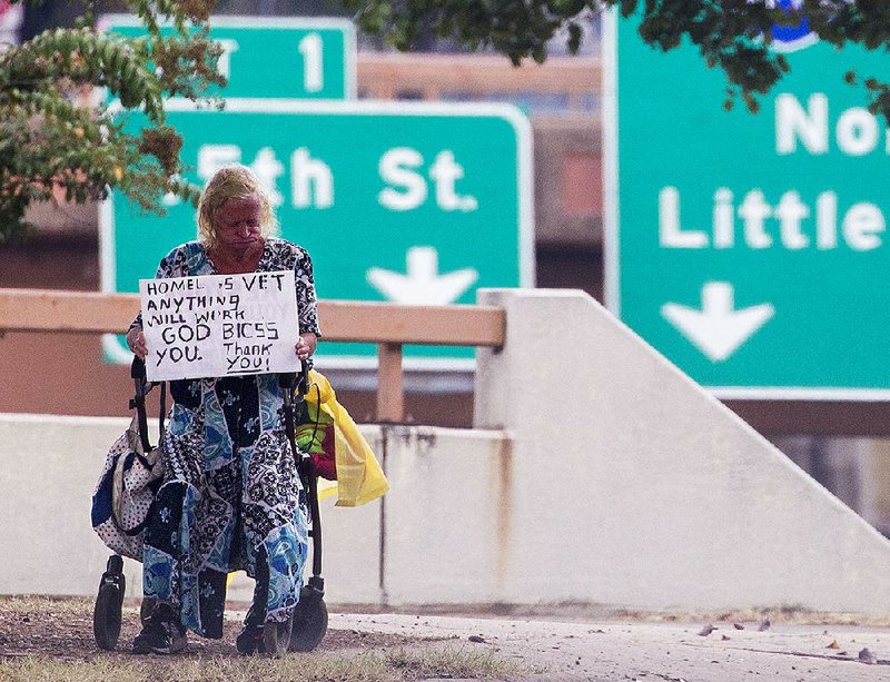 In this file photo a woman who asked not to be identified holds a sign asking for money Wednesday at the Main Street exit of Interstate 630 in Little Rock.