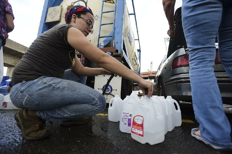 A municipal worker in Bayamon, Puerto Rico, fills water jugs for residents Thursday outside a stadium. People are desperate for food and water and items such as tarps to cover damaged roofs. 