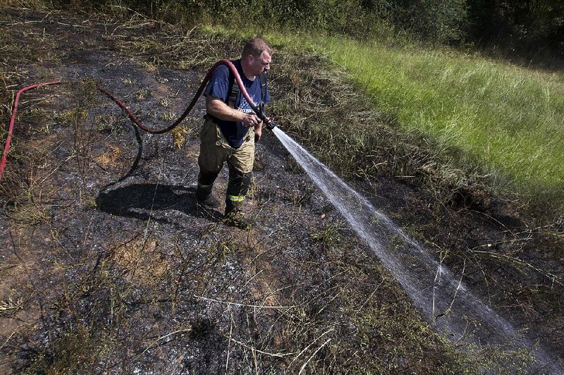 North Pulaski Fire District 15 volunteer Capt. Marcus Steele puts out a brush fire Thursday off Gribble Road in Jacksonville that started after winds blew embers from a tree stump a homeowner was burning into woods behind the home. 