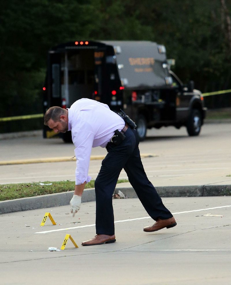 A Pulaski County sheriff’s office investigator picks up evidence markers Thursday in the parking lot near an apartment complex just outside the North Little Rock city limits where a Jacksonville man was fatally shot early Thursday during a carjacking. 