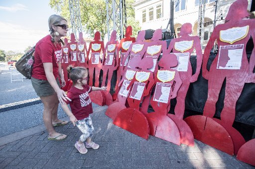 Stephannie Baker (CQ) with Moms Demand Action, looks at the 31 silhouette cutouts that symbolize the number of deaths by domestic violence in Arkansas in 2017, Friday Oct. 6, 2017 with her daughter Liza Baker , 4, on the Square in downtown Bentonville. To kick off the Silent Witness Project, Nathan Smith, Benton County Prosecutor, give a proclamation against domestic violence during First Friday in front of the Benton County Courthouse.