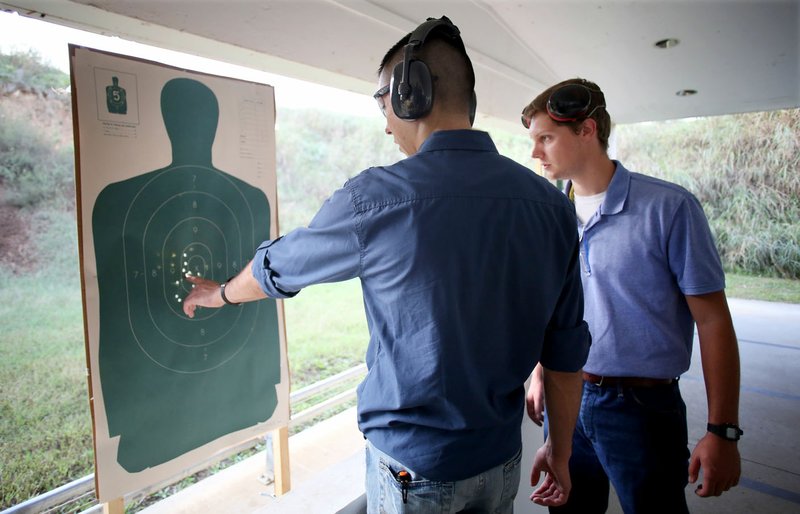 NWA Democrat-Gazette/DAVID GOTTSCHALK Cesar Barrientos (left) and Caleb Hall, both juniors at the University of Arkansas and interns with the Washington County Sheriff's Office, discuss Barrientos' target pattern Thursday following a round of live fire at the training facility at the Sheriff's Office in Fayetteville.