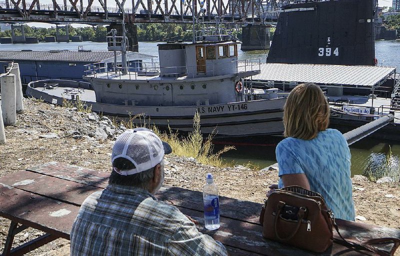 Danny and Karen Ridgon of Odessa, Mo., rest in the shade Saturday with the USS Hoga in the background in North Little Rock. The historic tugboat survived the Dec. 7, 1941, attack on Pearl Harbor, and its crew helped fight fires on the battleship Arizona and rescued sailors.