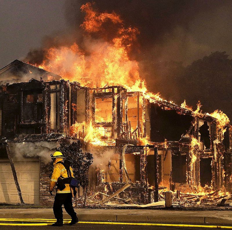 A firefighter keeps an eye on fire consuming a home Monday in Santa Rosa, Calif.
