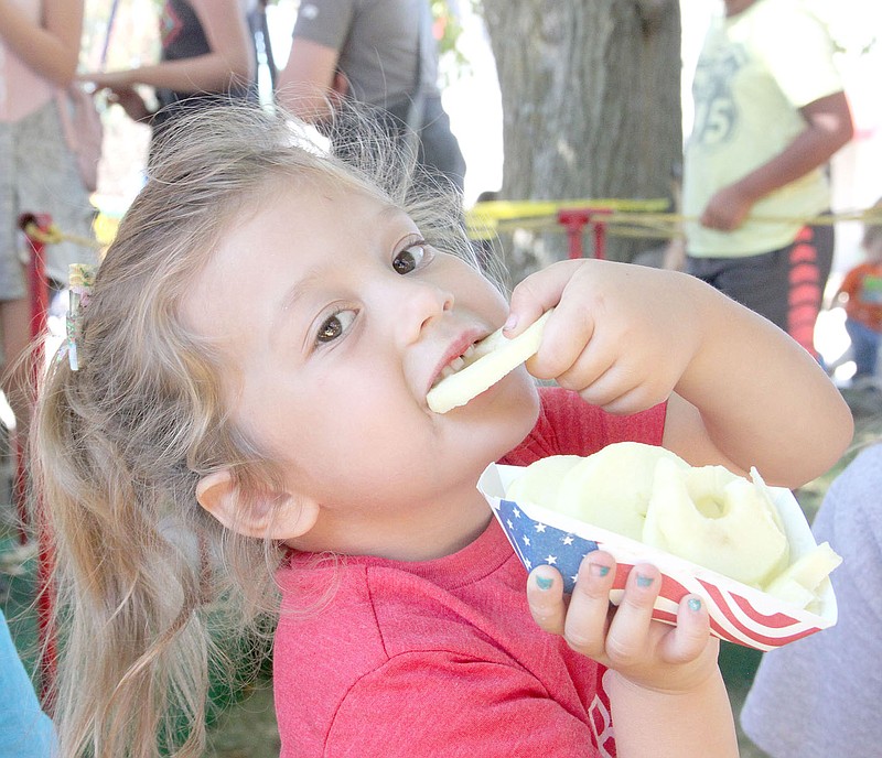 LYNN KUTTER ENTERPRISE-LEADER Abbi Lee, 4, of Farmington, enjoys a fresh slice of apple at the Arkansas Apple Festival in Lincoln. Volunteers under the red and white striped tent at the festival stayed busy peeling, slicing and handing out baskets of free apple slices to visitors.