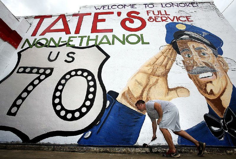 Trae Reed paints the curb Monday in front of a mural he recently finished painting at Tate’s Station in Lonoke. Reed is part of a group calling itself Lonoke 150 that donated time and about $800 worth of paint and supplies to put up the mural and paint the gas station. “A little bit of paint can go a long way,” Reed said. 