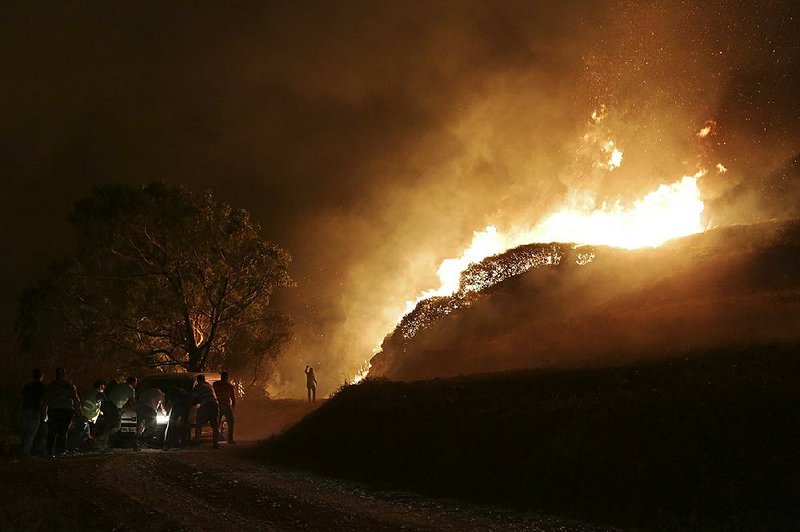 People push a van that got stuck carrying water for volunteers to fight a wildfire near houses in the outskirts of Obidos, Portugal, early Monday.