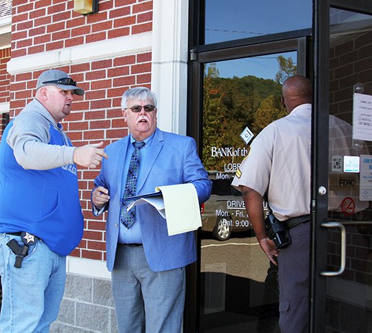 The Sentinel-Record/Grace Brown Garland County sheriff's Cpl. Josh Cannon, left, speaks with sheriff's Investigator Terry Threadgill following a robbery at Bank of the Ozarks, 3650 Highway 7 north, near Hot Springs Village, on Monday. An unidentified white man with his face partially covered with a surgical mask reportedly robbed the bank at around 9:30 a.m. Monday and left on foot. Photos of suspect inset in story.