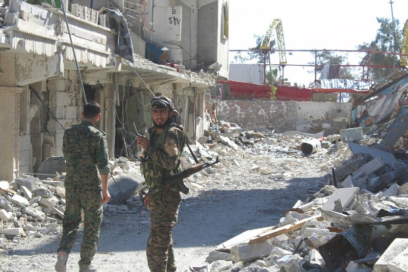 In this picture taken on Monday, Oct. 16, 2017, and provided by The Syrian Democratic Forces, a U.S.-backed Syrian Kurdish forces outlet that is consistent with independent AP reporting, shows Syrian Democratic Forces fighters, stand on destroyed street where they battle against the Islamic State militants, in Raqqa, Syria. 