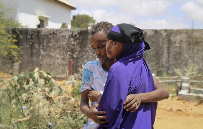 Zakariye Abdirisaq, left, who lost both his father and aunt in the bombing, is comforted by his cousin as they stand next to his father's grave, at a cemetery in Mogadishu, Somalia Tuesday, Oct. 17, 2017. Anguished families gathered across Somalia's capital on Tuesday as funerals continued for the more than 300 people killed in one of the world's deadliest attacks in years, while others waited anxiously for any word of the scores of people still said to be missing. (AP Photo/Mohamed Sheikh Nor)
