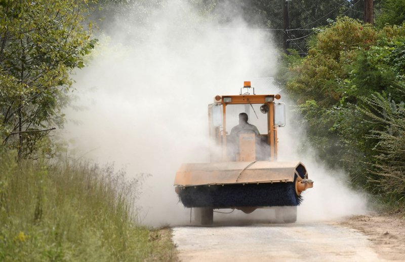 NWA Democrat-Gazette/FLIP PUTTHOFF John Evans with the Benton County Road Department drives out of a dust cloud Sept. 12 while sweeping dirt off La Faye Drive in the Monte Ne community near Rogers.