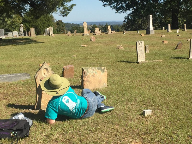 NWA Democrat-Gazette/LAURINDA JOENKS Abby Burnett of Kingston lies on the ground for a different perspective to photograph a tombstone in the Pleasant Grove cemetery in Scott County near Waldron. Burnett loves spending time in cemeteries, discovering and recording unusual grave markers. Here, she takes a picture of a baby carved into a head stone by A. Pitasky.