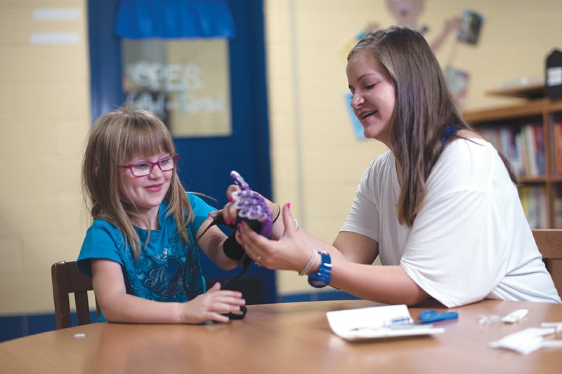 Emma Kincaid, left, practices using her new prosthetic hand designed and 3-D printed by Bryant High School junior Gracie Kimbrell, right. Gracie aspires to be a biomedical engineer, and she worked on Emma’s prosthesis with the help of teacher John Williams and an online community at enablingthefuture.org.