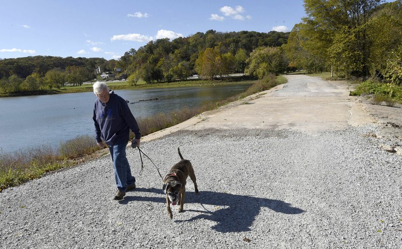 John Finch of Rogers and his dog, Samantha, walk Tuesday across Lake Bella Vista dam. Some want the dam removed. Others want to see it repaired. Bentonville’s City Council accepted a $98,960 grant from the Walton Family Foundation on Tuesday so the city could hire Ecological Design Group for $29,250 and the Watershed Resource Conservation Center for $63,960 to study three options to develop or change the lake and surrounding grounds.