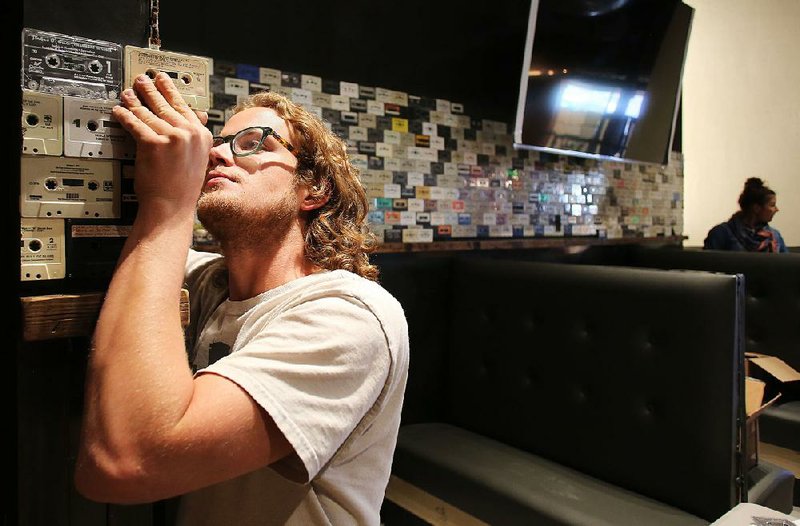 Alex Belto, with Little Rock-based Dave Grundfest Co., assembles an audiocassette tape facade on a wall of the new Big Orange restaurant at the Pinnacle Hills Promenade in Rogers earlier this month.