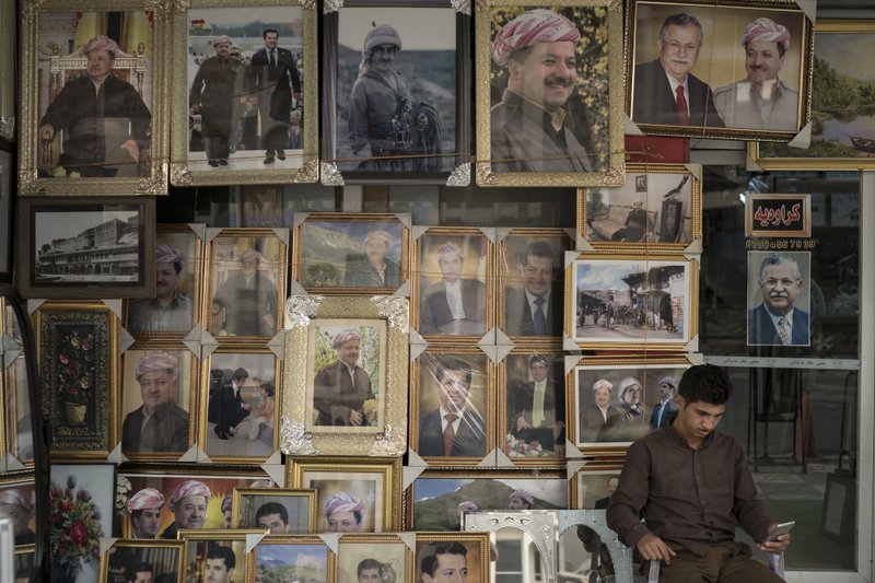 A man sits outside a store selling photos of Kurdish President Masoud Barzani and members of his family, in central Irbil, Iraq, Sunday, Oct. 29, 2017.