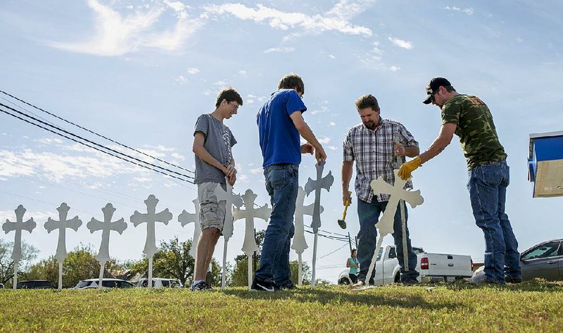 Zachary Kubena (from left), Doug John and his son Shelby John set up a memorial of 26 metal crosses near First Baptist Church in Sutherland Springs, Texas, on Monday.
