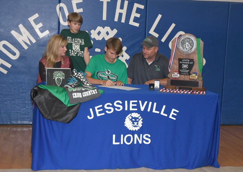 The Sentinel-Record/Mara Kuhn BISON BOUND: Jessieville's Noah Eskew, center, inks his national letter of intent to run cross country and track for Oklahoma Baptist University Friday in the Jessieville Sports Arena. Pictured with the senior are, l-r, his mother Tami Eskew, brother Kaleb Eskew, 11, and father Cory Eskew.