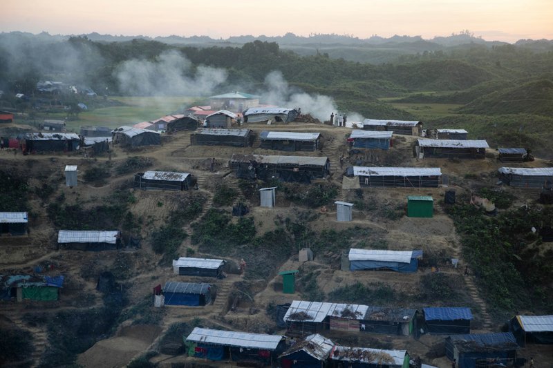 Rohingya Muslims stand, as smoke emits from the Hakim Para refugee camp in Ukhiya, Bangladesh Monday, Nov. 13, 2017. More than 600,000 members of the Muslim minority have fled to Bangladesh since August, when Rohingya insurgents attacked Myanmar police and paramilitary posts, and security forces responded with a scorched-earth campaign against Rohingya villages. (AP Photo/A.M. Ahad)