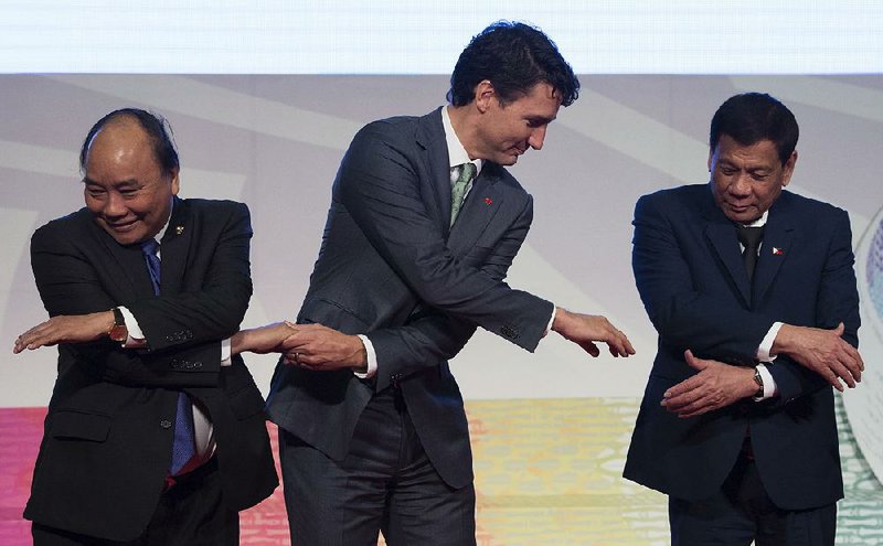 Canadian Prime Minister Justin Trudeau (center) reaches for the hand of Philippine President Rodrigo Duterte as they and Vietnamese Prime Minister Nguyen Xuan Phuc take part in a photo session Tuesday at the end of the Association of Southeast Asian Nations meeting in Manila. 