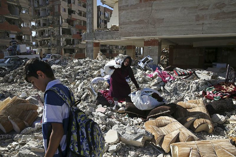 An earthquake survivor on Tuesday carries belongings over debris at a government housing compound where she lived in Sarpol-e-Zahab, Iran. 
