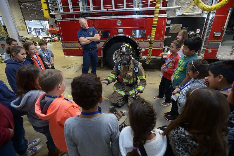 NWA Democrat-Gazette/ANDY SHUPE
Third-graders from Decatur listen Wednesday, Nov. 15, 2017, as Marty Striefler (center) and Dave Harrison (left), both firefighters with the Fayetteville Fire Department, describe the personal protective equipment they use in their work as students tour the department's central fire station in downtown Fayetteville. The students are gaining experience about many occupations through the Operation Dream Big program and toured a bank and a studio.