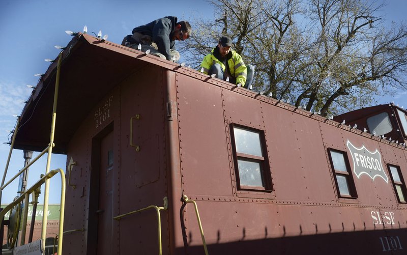 NWA Democrat-Gazette/ANDY SHUPE Josh Scarbrough (left) and Levi Roper, both with The Lighting Master, work together Thursday while decorating the caboose in Rogers' Frisco Park with holiday lights. Themed "Hollywood Christmas" this year, the city's annual Christmas parade is planned from 7 to 9 p.m. Dec. 1 and features an appearance by Santa Claus.