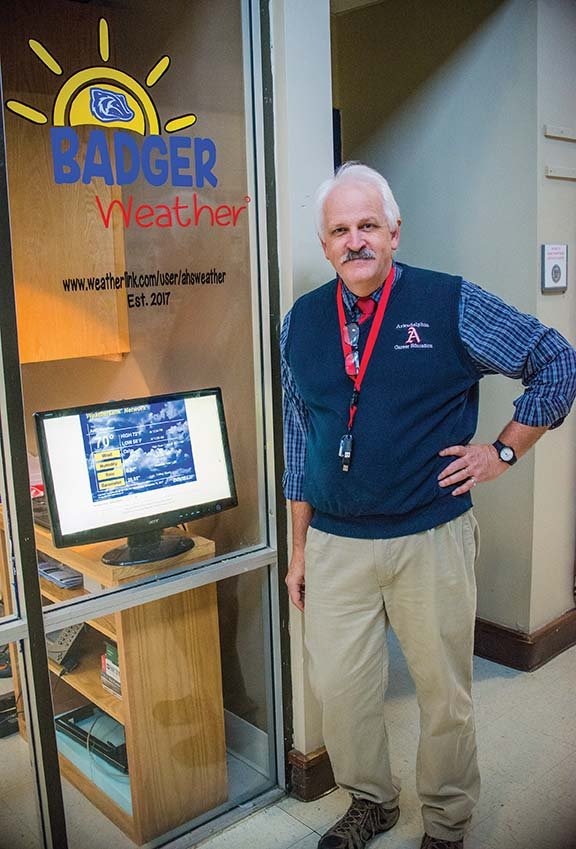 Bud McMillion, the pre-engineering teacher at Arkadelphia High School, stands next to the new Badger Weather Station monitor in the hallway of the school. McMillion said the station gets more accurate readings than most phone apps. 