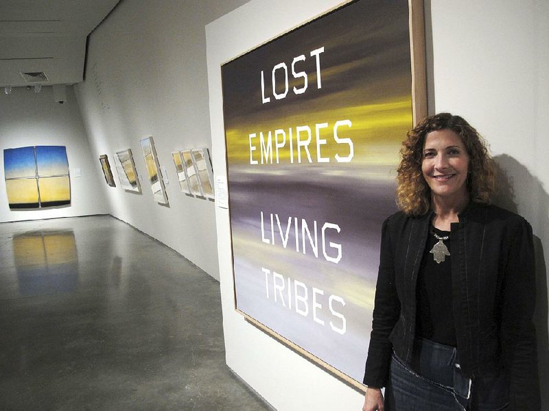 JoAnne Northrup, curator for contemporary arts at the Nevada Museum of Art, poses next to a work by American artist Ed Ruscha in “Unsettled,” an exhibit that looks at the “Greater West” region. The exhibit is on display in Reno, Nev.