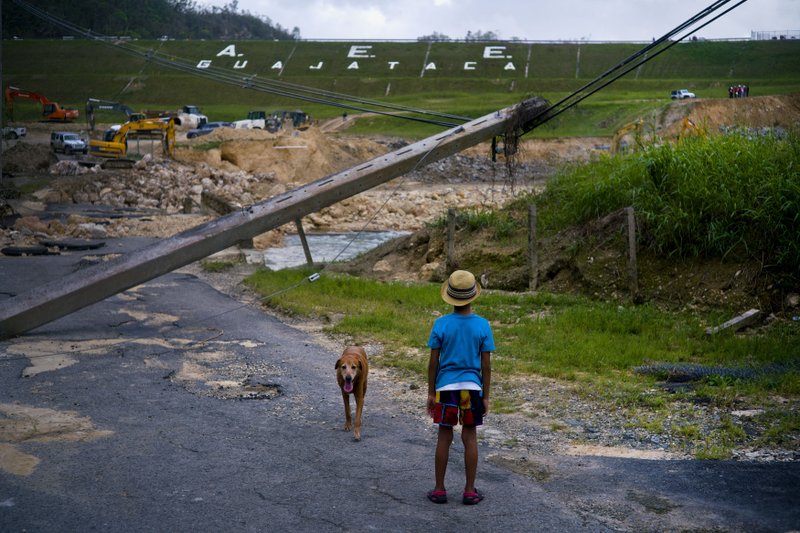 FILE - In this Oct. 17, 2017 file photo, a boy accompanied by his dog watches the repairs of Guajataca Dam, which cracked during the passage of Hurricane Maria, in Quebradillas, Puerto Rico. Experts said on Thursday, Nov. 16, 2017, that Puerto Rico could face nearly two decades of further economic stagnation and a steep drop in population as a result of Maria. (AP Photo/Ramon Espinosa, File)